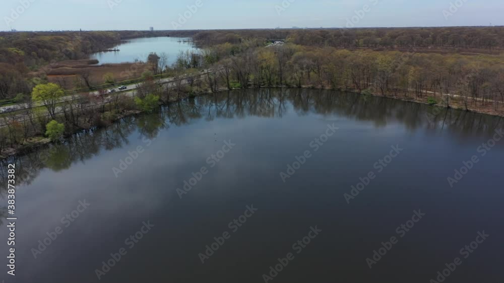 An aerial view of some reflective lakes during the day. The drone camera hovers and pan left over one of the lakes. The parkway ahead has some automobile traffic which is moderate. An aerial view of some reflective lakes during the day. The drone camera hovers and pan left over one of the lakes. The parkway ahead has some automobile traffic which is moderate.