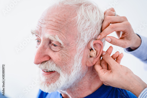 Doctor helps mature male patient to use hearing aid. Close up photo of a senior man smiling while using hearing aid.