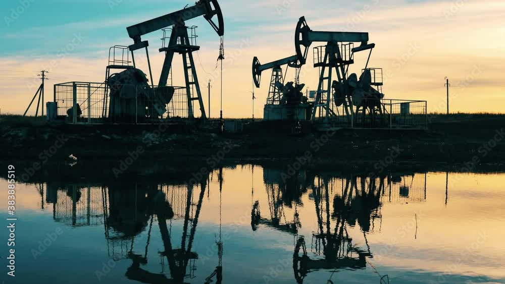 Sunset with multiple metal constructions pumping oil. Oil well, crude oil, drilling rig, oil field, crude oil price, oil and gas, oil barrel, oil industry concept.