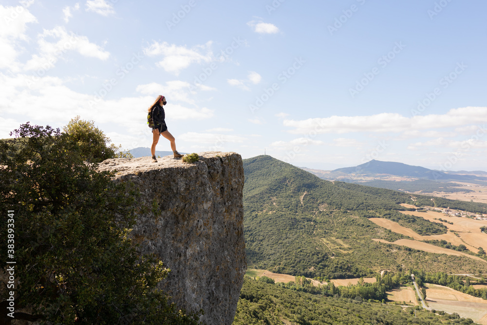 Chica adolescente con mascarilla mirando hacia el horizonte al borde de un precipicio en la montaña