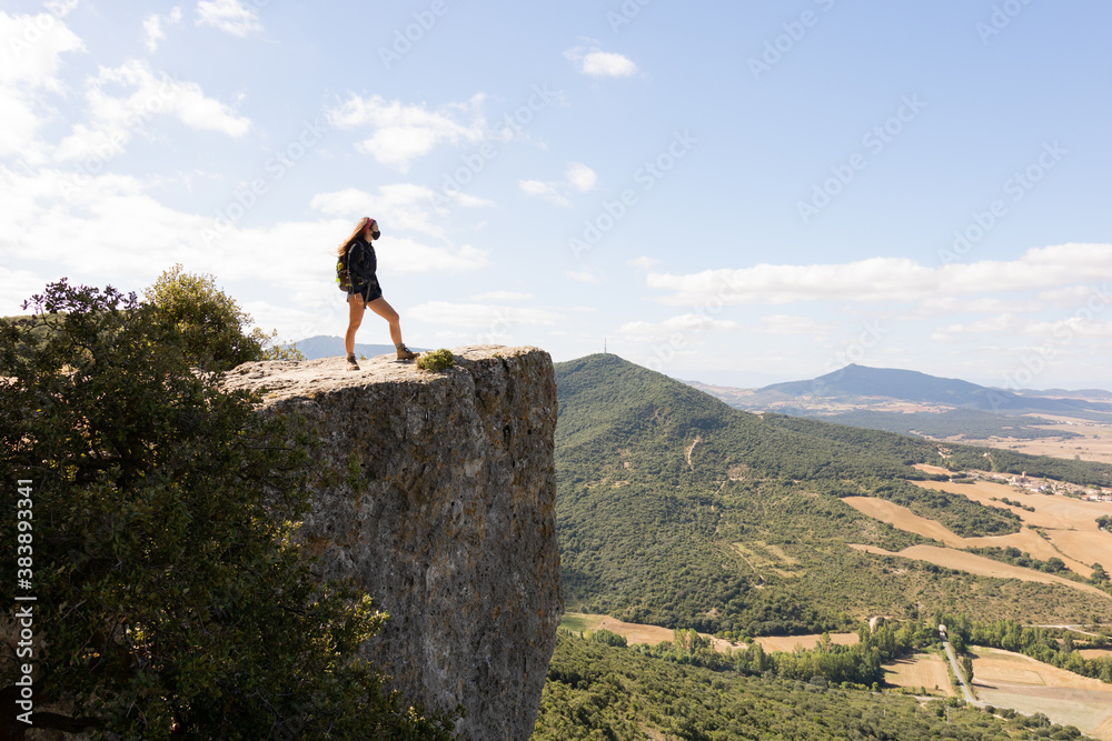 Chica adolescente con mascarilla mirando hacia el horizonte al borde de un precipicio en la montaña Chica adolescente con mascarilla mirando hacia el horizonte al borde de un precipicio en la montaña