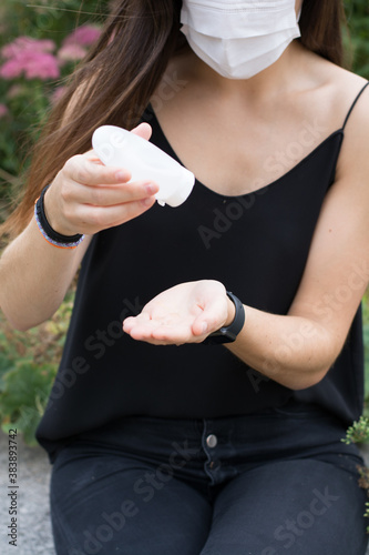 A woman disinfecting her hands in a park, using a face mask. 