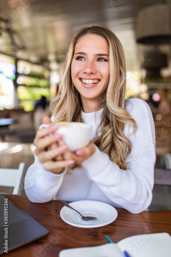 Portrait of young woman drinking coffee at table in cafe