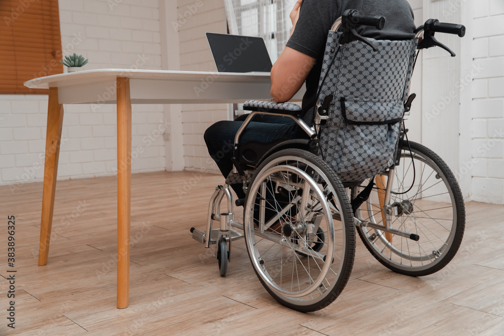 Obraz premium Happy disabled Asian man sitting in a wheelchair And working with computer at home, The concept of Technologies for the convenience of people with disabilities.