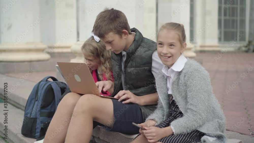 Side view of generation Z children surfing Internet on devices on school break. Absorbed schoolchildren using social media on smartphone, laptop, and tablet. Side view of generation Z children surfing Internet on devices on school break. Absorbed schoolchildren using social media on smartphone, laptop, and tablet.