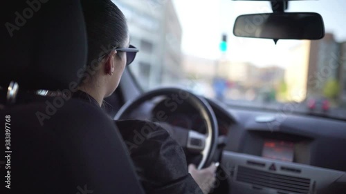 Woman driving car fast in city street with traffic. Road trip, speeding, escape or chase concept. Commuter, female taxi cab driver or ride share person. Interior back view of cockpit. Summer lifestyle