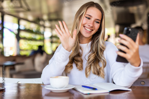 Cheerful woman taking picture on smartphone camera for share in social networks sitting in cafe. Smiling woman using cellular an accessory making video call satisfied with wifi in cafe