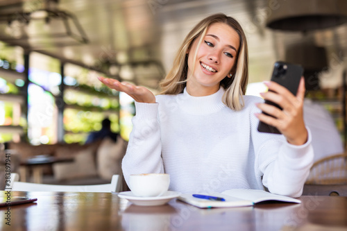 Cheerful woman taking picture on smartphone camera for share in social networks sitting in cafe. Smiling woman using cellular an accessory making video call satisfied with wifi in cafe