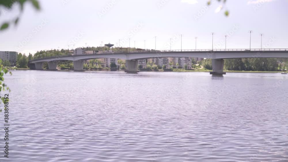 Lake and bridge in Jyvaskyla, Finland. Beautiful Finnish landscape and city view in Scandinavia. Scenic nature on a sunny summer day. Camera movement behind birch tree leaves. Lake and bridge in Jyvaskyla, Finland. Beautiful Finnish landscape and city view in Scandinavia. Scenic nature on a sunny summer day. Camera movement behind birch tree leaves.