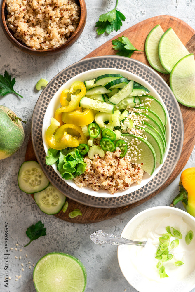 Burrito bowl with quinoa and green vegetables. Salad of quinoa, cucumber, peppers, radishes and celery in a bowl on gray concrete background top view. Healthy diet food, vegetarian food.