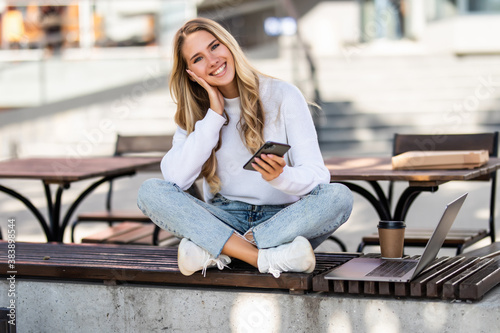 Young smiling woman using smartphone sitting on bench in park.