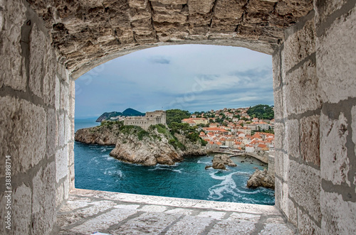 View from stone window of Lovrijenac  fortress surrounded by blue sea and red rooftops and roofs of historic buildings of Dubrovnik. Beautiful fort on cliffs and rocks. photo
