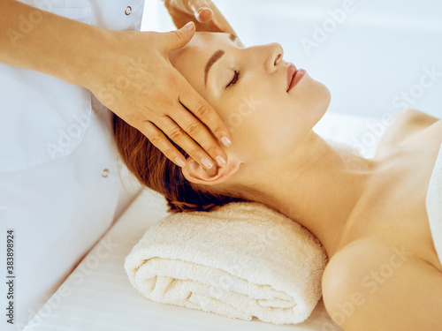 Beautiful woman enjoying facial massage with closed eyes in spa center. Relax treatment concept in medicine