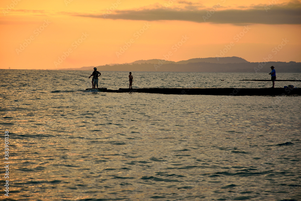 Fishermens on the sea pier during the summer sunset.
