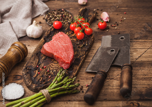 Slice of Raw Beef sirlion steak on wooden chopping board with tomatoes,garlic and asparagus tips and meat hatchets. photo