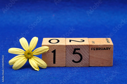 15 February on wooden blocks with a yellow flower on a blue background