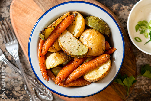 Baked vegetables. Roasted potatoes, carrots and radish with herbs in a bowl on a dark background top view. Vegetarian food, rustic style. © Светлана Монякова