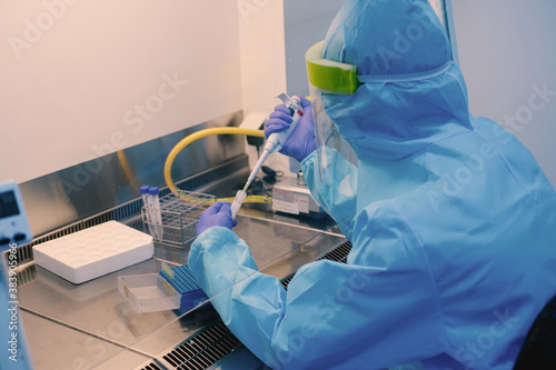 A scientist in PPE safty uniform pipetting sample experiment in biological safety cabinet (BSC).