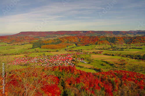 Hiking through colorful forests and old woods  green farm fields and small villages seen from uphill in golden Autumn colors in South Germany.