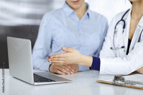 Unknown woman- doctor and her patient are discussing patient's blood test, while sitting together at the desk in the cabinet in a clinic. Female physician, with a stethoscope, is using a laptop © rogerphoto