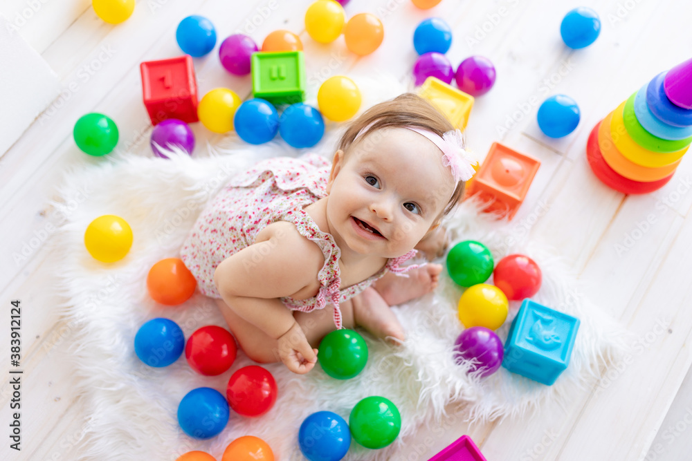 Obraz premium happy little girl sitting in a white room in a red dress with bright toys and looking at the top