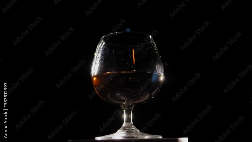 Pouring brandy or cognac from the bottle into the glass against wooden background. Slow motion. Pouring brandy or cognac from the bottle into the glass against wooden background. Slow motion.