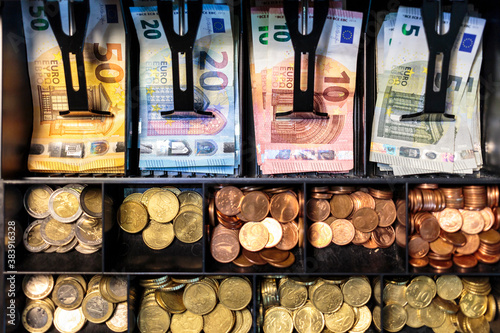 Open money drawer of a register in a European small business. Top view of bills organized into slots of a cash tray, with banknotes of 50, 20, 10 and 5 Euros, and coins of all Euro Zone denominations