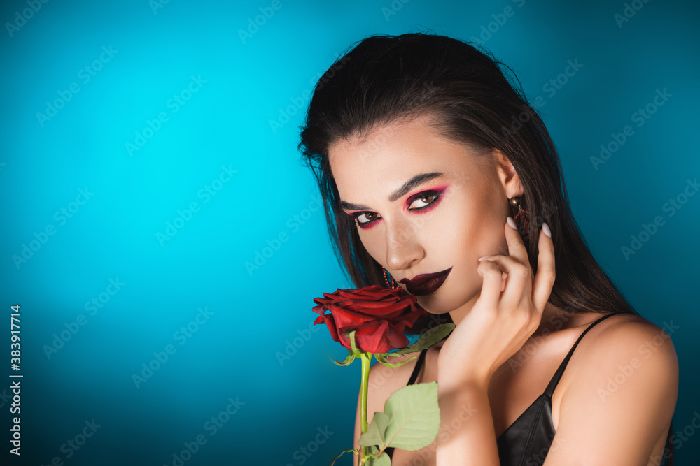 young woman with black makeup near red rose on blue