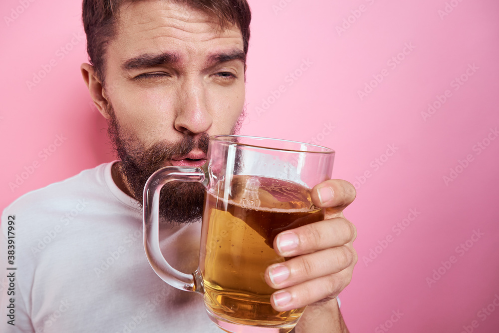 Drunk man with a large mug of beer On a pink background and a white T-shirt relaxed view of a thick beard 