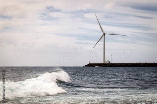 Horizontal View Of Ocean Waves And A Very Large Wind Turbine Next To The Sea In The Coastal Town Of Arinaga, Island of Gran Canaria, In The Spanish Canary Islands
