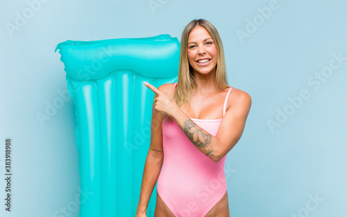 pretty woman wearing swimsuit smiling cheerfully, feeling happy and pointing to the side and upwards, showing object in copy space