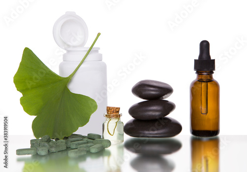 Pills with extract from the ginkgo in bottle and green leaves isolated on a white background.
