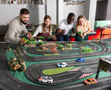 Friendly team of young men and women is playing with slot car model racing track indoor