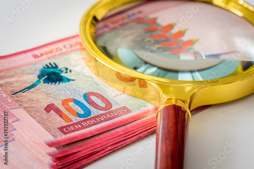 A bundle of Bolivian banknotes of one hundred Bolivianos with a magnifying glass on it. The concept of currency fluctuations and difficult economic situation photo