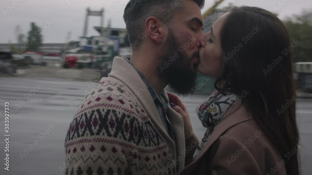 Middle-aged man and woman in love kissing on the street of a busy city in autumn in cloudy weather. A man in a sweater kissing a woman in a coat.