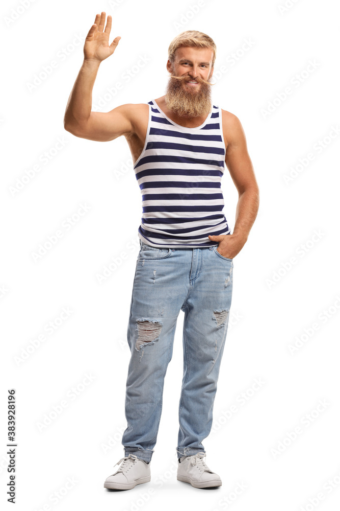 Full length portrait of a blond guy with beard and mustache wearing a striped vest and jeans and waving at the camera