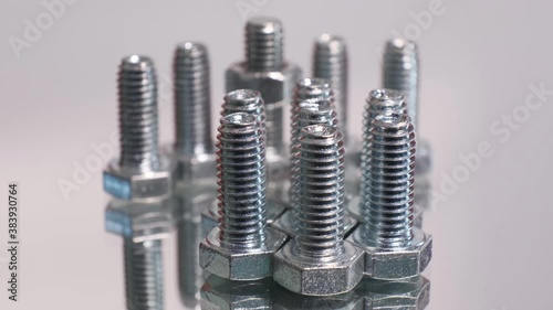 Rotating group of galvanized metallic screws close-up. Stainless steel bolts isolated on white mirror reflective background.