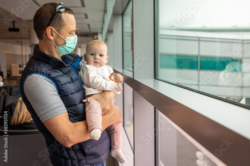 Father in medical mask and his daughter small baby girl waiting a boarding on plane at the airport in Prague, Czech republic, Europe