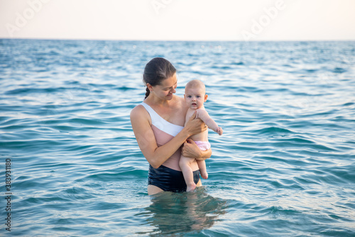 Beautiful young woman with her daughter little baby girl swimming in the sea at sunset time. Woman with daughter relaxing in front of sea