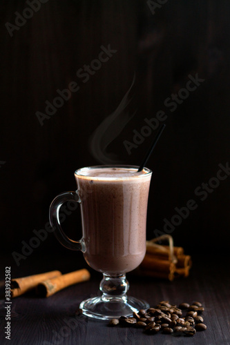 hot drinks winter and autumn. cup of hot chocolate. glass of hot cocoa with whipped cream, coffee beans and cinnamon sticks on a dark background. hot drinks on a wooden background. vertical.copy space
