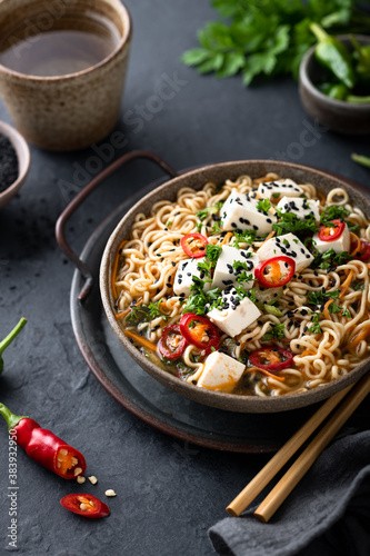 Asian noodle soup, ramen with tofu and vegetables in ceramic bowl on dark background, selective focus