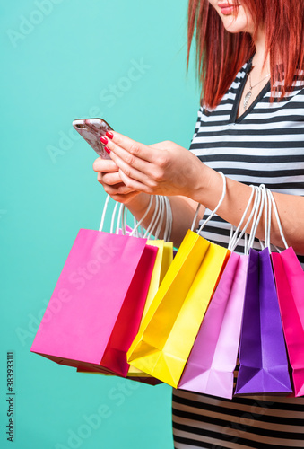 Woman shopping and using a smartphone. Red hair woman holding shopping bags.