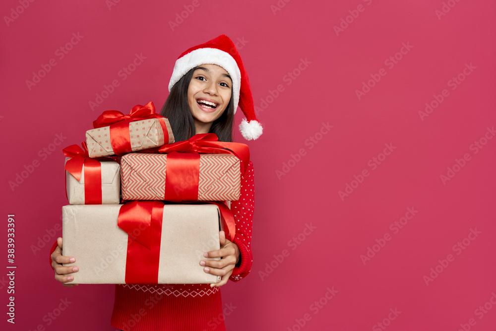 Excited funny indian latin kid child girl wears santa hat looking at camera holding many gifts boxes celebrating happy 2021 New Year isolated on red background. Merry Christmas presents shopping sale. Excited funny indian latin kid child girl wears santa hat looking at camera holding many gifts boxes celebrating happy 2021 New Year isolated on red background. Merry Christmas presents shopping sale.