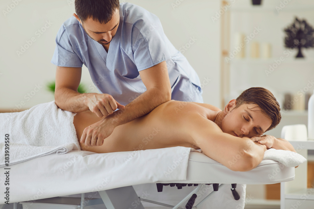 Obraz premium Relaxed young man enjoying professional body massage in spa salon or health center