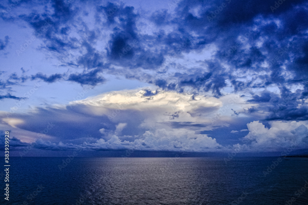 Obraz premium Panoramic view of ocean waters horizon line with dramatic cumulus thunderstorm cloudscape in blue sky background.