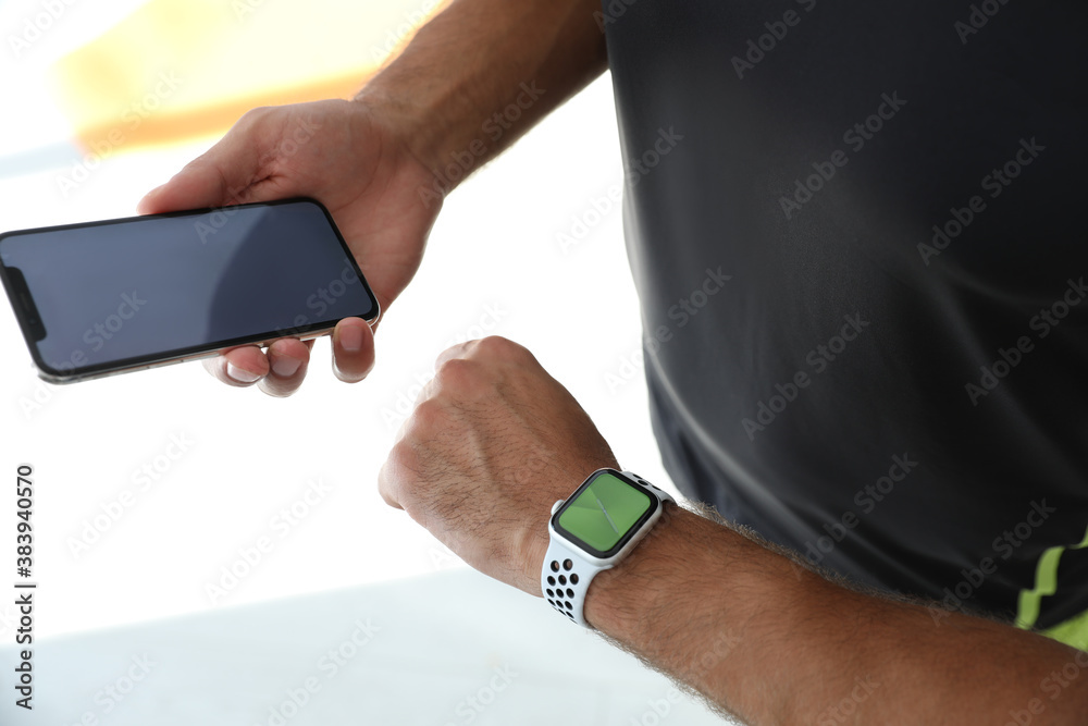 Man with smartphone checking fitness tracker in gym, closeup
