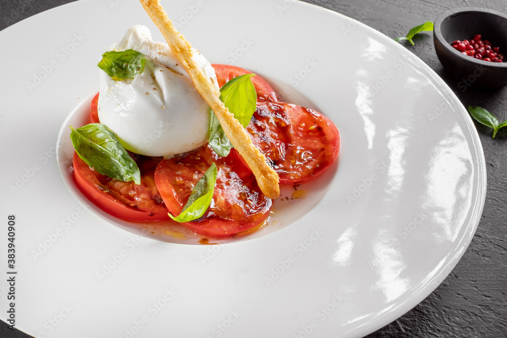 Burrata cheese and tomato salad with Basil and olive oil served on a white plate Burrata cheese and tomato salad with Basil and olive oil served on a white plate