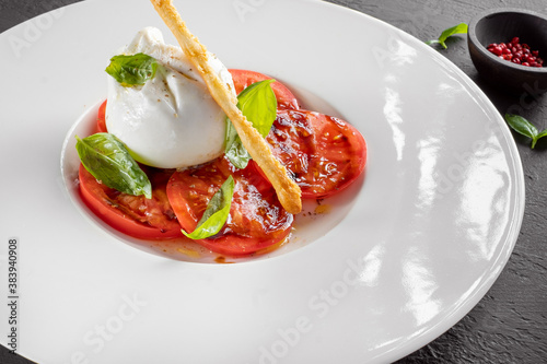 Burrata cheese and tomato salad with Basil and olive oil served on a white plate