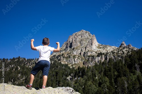 Young boy doing the victory gesture looking at a big mountain