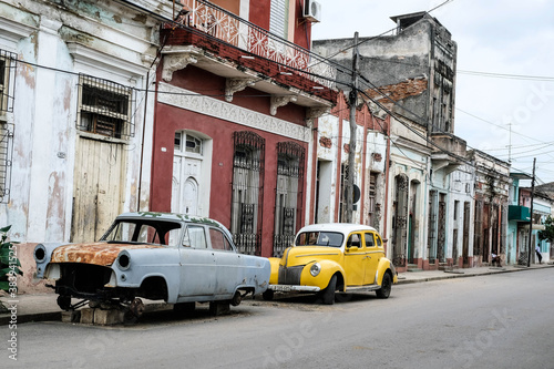 small yellow car and broken blue car parked on the street in cuba © Musa